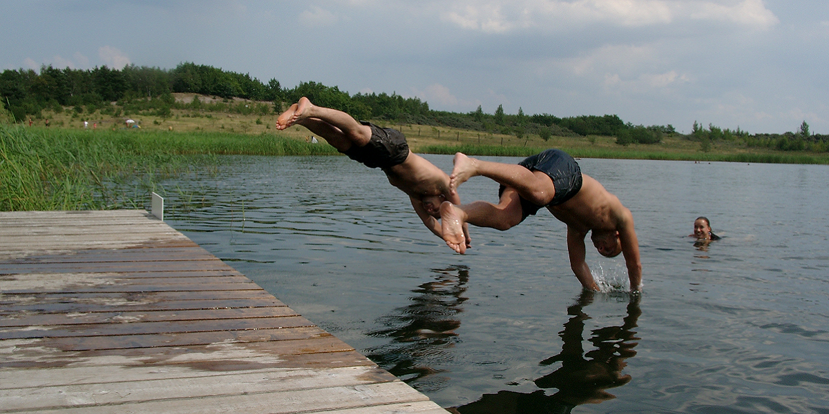 Bild: Zwei Jungen machen von einem Holzsteg aus einen Kopfsprung ins Wasser.