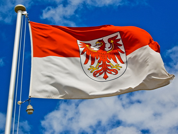 Die Brandenburg-Flagge weht an einem Fahnenmast vor blauem, wolkigem Himmel.
