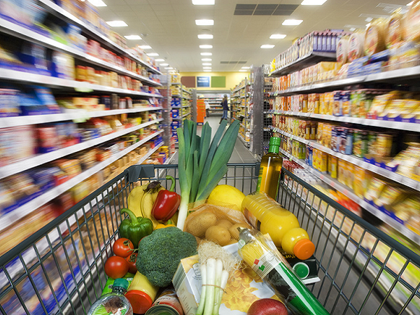 Angebot im Supermarkt Ein mit Lebensmitteln gefüllter Einkaufswagen steht zwischen den Einkaufsregalen.