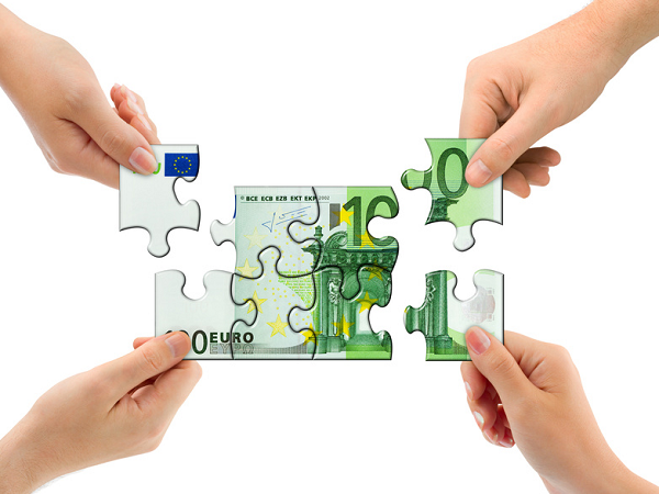 100 Euro-Schein als Puzzle, der jeweils an den Ecken von Händen festgehalten wird.