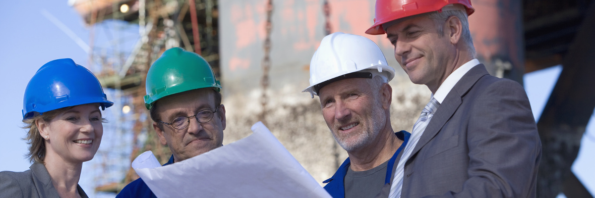 Menschen mit Schutzhelmen auf einer Baustelle betrachten Baupläne.