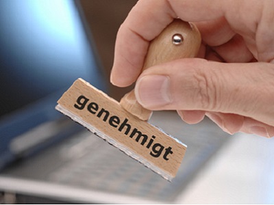 Eine Hand hält einen Stempel mit der Aufschrift 'genehmigt'